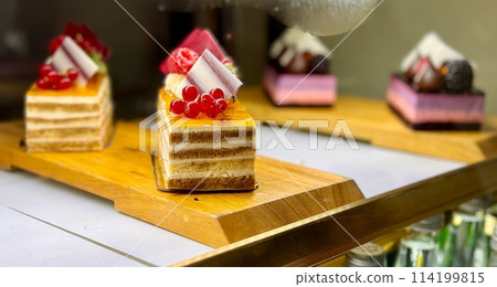A portion of layered cream yellow cake with red raspberries, red currants on a wooden stand on the counter of the restaurant. Close-up A portion of layered cream yellow cake with red raspberries, red currants on a wooden stand on the counter of the restaurant. Close-up 114199815