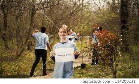 Portrait of sweet girl with save our planet poster against pollution and illegal dumping, volunteering to restore and preserve nature in the forest. Little child shows awareness sign. Camera B. 114200131