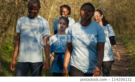 Satisfied people leaving the woods after a productive litter cleanup session, being successful in cleaning the forest environment from junk and plastic waste. Happy proud activists. Camera A. 114200132