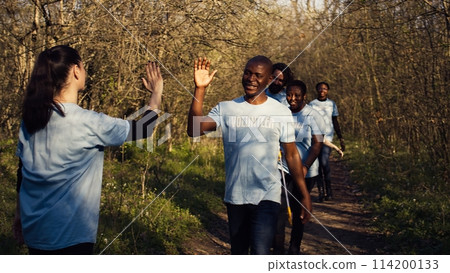 Activists congratulating each other with a high five after a successful teamwork, showing perseverance in collecting rubbish and plastic waste from forest environment. A job well done. Camera B. 114200133