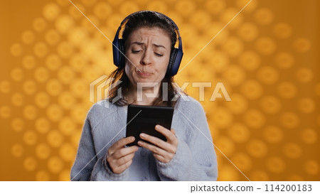 Voice actor frowns while reading ebook, portraying character, studio background. Woman reenacting digital recording of novel, interpreting furious antagonist, reading text from tablet, camera B Voice actor frowns while reading ebook, portraying character, studio background. Woman reenacting digital recording of novel, interpreting furious antagonist, reading text from tablet, camera B 114200183