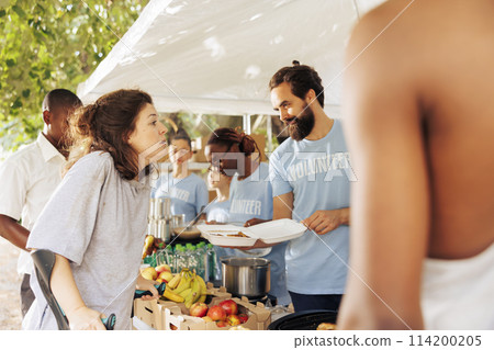 Image shows caucasian woman on crutches receives assistance from multicultural volunteers for hunger relief. Free food and humanitarian aid provided to needy and crippled by non-profit organization. 114200205