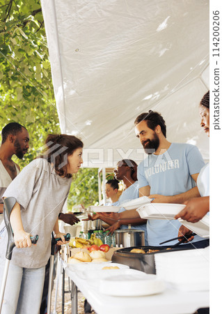 Multiethnic charity group gives back, providing free food, shelter, and support to the less fortunate. Smiling and happy volunteers helping the homeless, sick, and disadvantaged individuals in need. 114200206