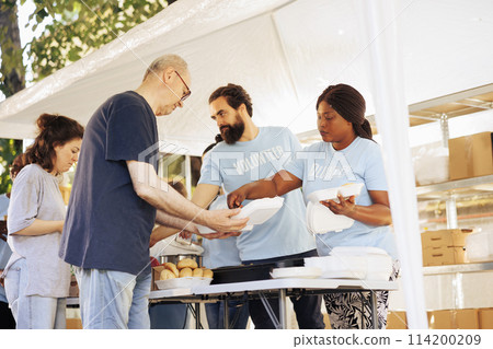 Multiracial team working together at food drive, charitably distributing essential items to less fortunate. Multiethnic people wearing blue t-shirts providing hunger relief and volunteer assistance. 114200209