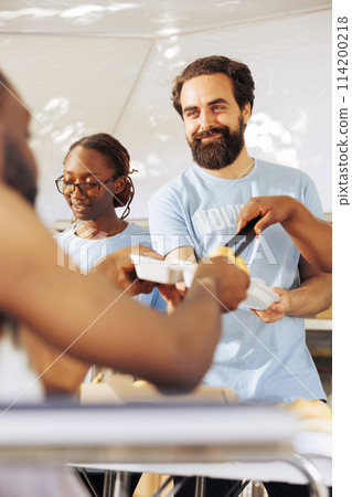 Portrait of a friendly volunteer distributing free food to a crippled homeless person. Detailed image shows a caucasian man helping during a food drive to serve hot meals to the poor and needy. Portrait of a friendly volunteer distributing free food to a crippled homeless person. Detailed image shows a caucasian man helping during a food drive to serve hot meals to the poor and needy. 114200218