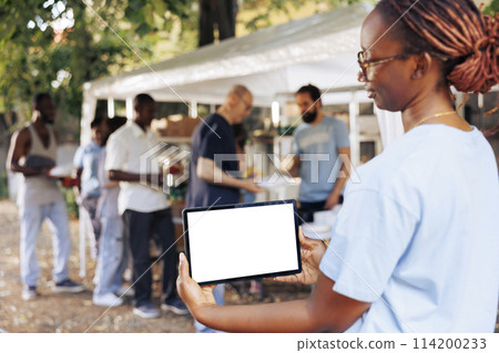 An isolated mockup template for philanthropic messages is held by young black woman holding a digital tablet. African american woman volunteer holding a smart device with a blank white screen display. 114200233
