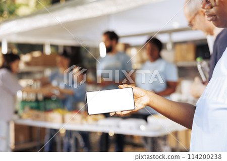 Black woman holding a cellphone with isolated mockup template for custom messages related to charity. African american female volunteers grasping digital device with blank white screen display. Black woman holding a cellphone with isolated mockup template for custom messages related to charity. African american female volunteers grasping digital device with blank white screen display. 114200238