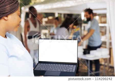 Detailed image showing african american female volunteer carrying laptop with isolated copyspace display for customization. Black woman holding minicomputer with white screen mockup template. 114200242