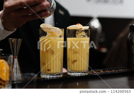 A bartender adds spices to a yellow cocktail. A bartender adds spices to a yellow cocktail. 114200563
