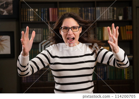 Portrait of an angry woman boss with glasses in the office looks at the camera and screams 114200705