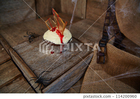 Halloween Themed Bloody Cupcake with Candy Glass and Spooky Decor on Aged Wood 114200960