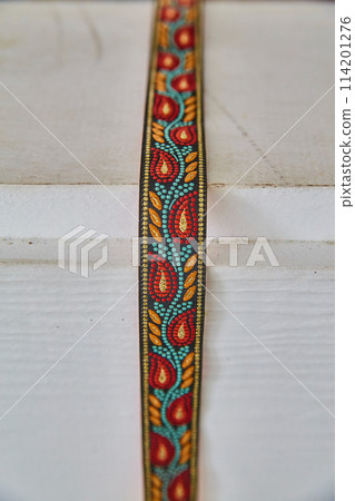 Intricate Embroidered Ribbon Pattern on White Wood 114201276