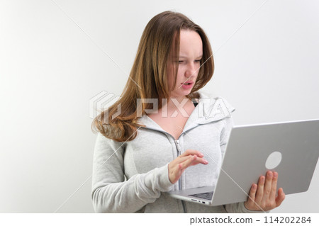 A young female student sitting at the table, using headphones when studying. 114202284