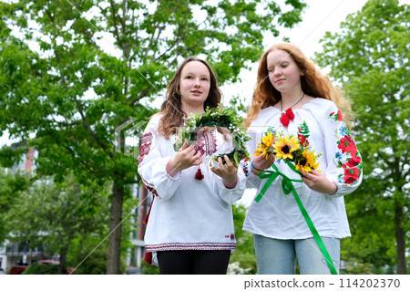 ancient Ukrainian traditions weaving wreaths on Ivan Kupala two girls with beautiful red hair during wind are preparing for evening sunset launching beautiful floral decorations embroidered shirts 114202370