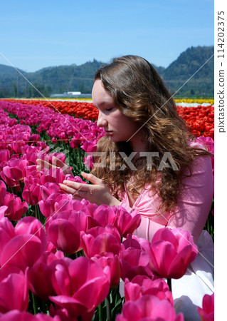 a young girl teenager stands in beautiful bright pink Corolla tulips inhale the fragrance of flowers straighten her hair look into the distance beautiful field in spring unusually bright color 114202375