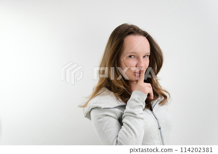 a young teenage girl puts her finger to her lips secrecy don't tell anyone sharply turn around look into the frame wave a finger negatively on a white background stern look a young teenage girl puts her finger to her lips secrecy don't tell anyone sharply turn around look into the frame wave a finger negatively on a white background stern look 114202381