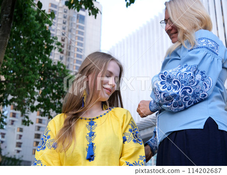 mother and daughter love mother straightens hair and takes her way migrants refugees Ukraine war in Ukraine aggression of Russia yellow vyshyvanka blue traditional clothes on street flag of Ukraine 114202687