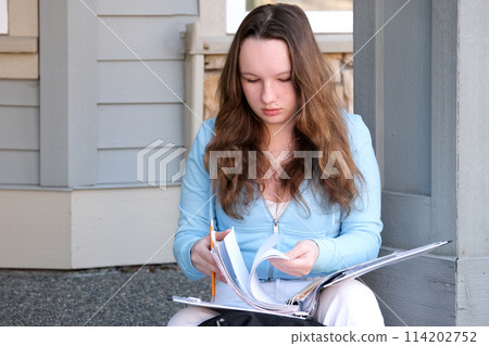young girl teenager sits on porch in hands with a folder, a magazine and pencil, do homework, solve problems, wait at the door, a beautiful woman, young white jeans, a briefcase, think, work, study 114202752