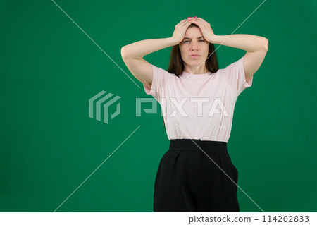 Portrait of concerned tired young woman in green casual clothes looking camera, putting hands on head isolated on bright blue wall background in studio. People lifestyle concept. Mock up copy space Portrait of concerned tired young woman in green casual clothes looking camera, putting hands on head isolated on bright blue wall background in studio. People lifestyle concept. Mock up copy space 114202833