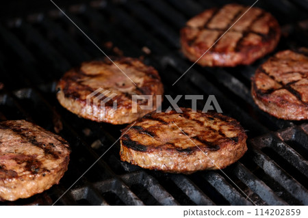 Hamburgers cooking on barbeque grill with flames On a grill are half fried minced meatballs for a homemade burger background for BBQ in the summer with charcoal and fresh meatballs 114202859