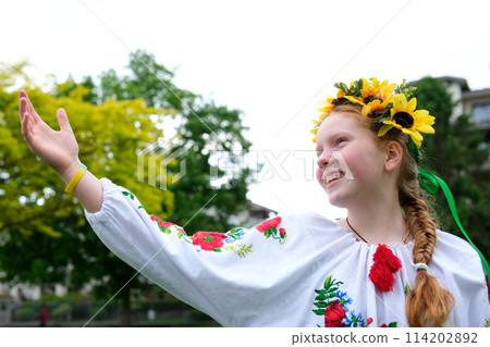young red-haired girl in a wreath of sunflowers outdoors in park garden in embroidered Ukrainian vyshyvanka shirt with red braid with ribbons in hair Ukraine Peaceful Time of happiness joy and peace young red-haired girl in a wreath of sunflowers outdoors in park garden in embroidered Ukrainian vyshyvanka shirt with red braid with ribbons in hair Ukraine Peaceful Time of happiness joy and peace 114202892