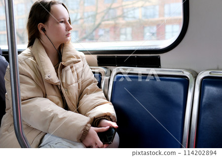 There is space for text Ukrainian fair haired European girl sits in skytrain and she listens to music in front of her holds the phone She is in a white blouse and blue ripped jeans she is in a tunnel There is space for text Ukrainian fair haired European girl sits in skytrain and she listens to music in front of her holds the phone She is in a white blouse and blue ripped jeans she is in a tunnel 114202894