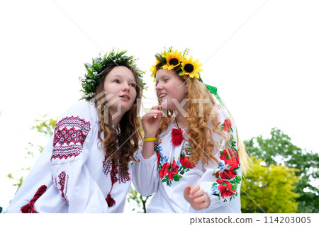 Midsummer. Two girls in the Slavic clothes weave braids in the hair near the fire. Midsummer. Two girls in the Slavic clothes weave braids in the hair near the fire. 114203005