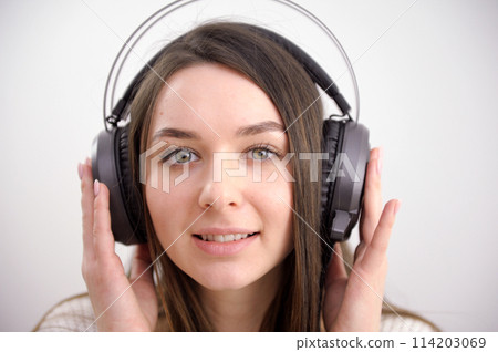 The girl in headphones young woman listening her favourite songs in headphones looking funny on isolated white background The girl in headphones young woman listening her favourite songs in headphones looking funny on isolated white background 114203069
