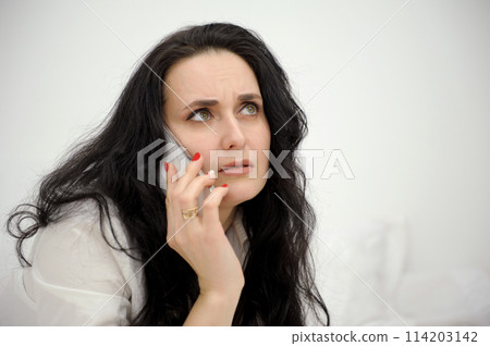 Worried young woman looks nervously, bites finger, isolated Female is nervous while talking on the phone, feels frustrated due to an awkward situation, feeling shame Worrying phone talk concept 114203142
