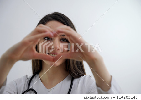 Cute Little Indian girl doctor examining Stuffed heart toy with stethoscope while wearing Doctor's uniform. Standing isolated over white background 114203145