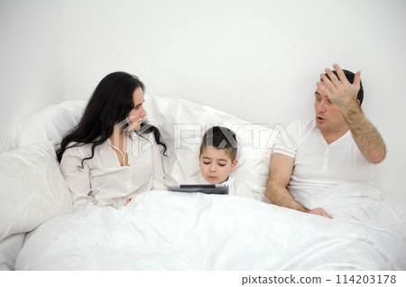home disagreements parents quarrel in bed under covers son boy with tablet psychological problems conflicts disagreements father and mother raised their hands and shouted at each other 114203178