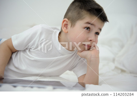 boy of seven or eight years old sits on bed leaned on arm lay down on white blanket looks into distance sly thoughtful look plans day Thinks about the prospects for future dreams desires black hair boy of seven or eight years old sits on bed leaned on arm lay down on white blanket looks into distance sly thoughtful look plans day Thinks about the prospects for future dreams desires black hair 114203284
