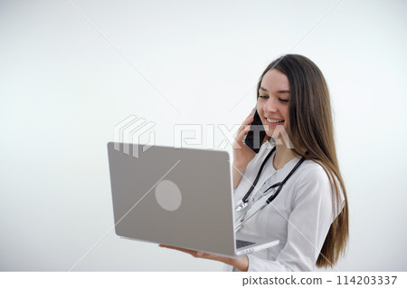 young doctor woman talking on phone and watching online conference laptop quarantine time treatment communication correction treatment on neck phalendoscope on white background studio space for text young doctor woman talking on phone and watching online conference laptop quarantine time treatment communication correction treatment on neck phalendoscope on white background studio space for text 114203337