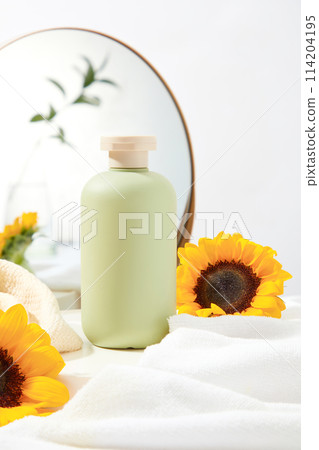 Blank green bottle stand on white table, surrounded by some bathroom products such as bath towel and mirror with sunflower as an accent. Space for design and front view Blank green bottle stand on white table, surrounded by some bathroom products such as bath towel and mirror with sunflower as an accent. Space for design and front view 114204195