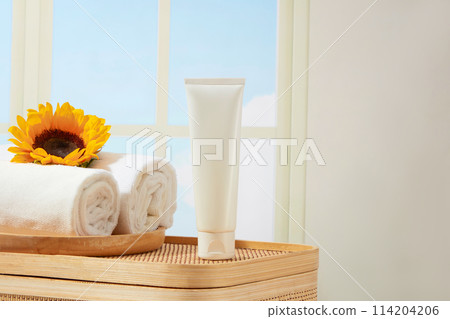 A rattan basket which used for storing bathroom items contains a empty label tube and a wooden tray of towels, decorated by a fresh sunflower. Photo for design promotion pics 114204206