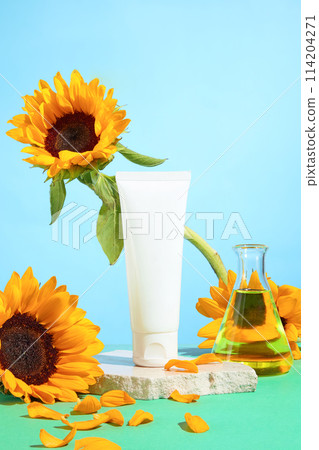 Blank label tube placed on white plaster podium, decorated by sunflower and lab glassware over light blue background. Space for advertising, front view 114204271