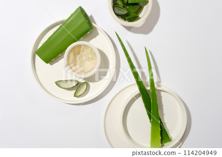 Top view of aloe vera decorated contained on several white porcelain dishes flat lay on white flat form. Photo for advertising product made by aloe, blank space for design 114204949