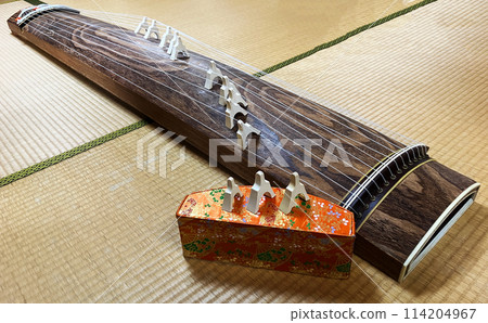 A traditional 13-stringed koto with bridges sits on the tatami mats of a Japanese-style room. The bridges and the overall picture A traditional 13-stringed koto with bridges sits on the tatami mats of a Japanese-style room. The bridges and the overall picture 114204967