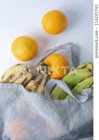 Fresh bananas and oranges in a reusable bag on a white background. 114205743