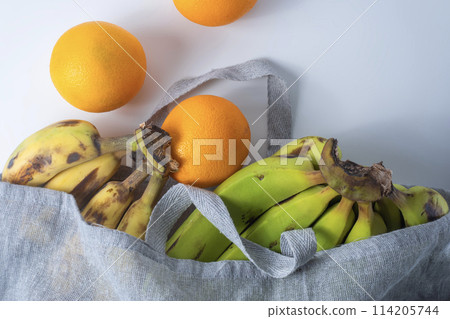 Fresh bananas and oranges in a linen bag on a white background. 114205744