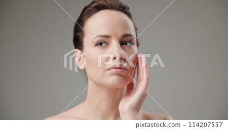 Beauty, health, cosmetics, anti-aging therapy and skin care concept - young beautiful brunette Caucasian woman touching face and looking at camera Beauty, health, cosmetics, anti-aging therapy and skin care concept - young beautiful brunette Caucasian woman touching face and looking at camera 114207557