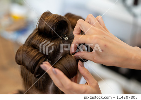 The hairdresser curls the model's hair. Curling iron for curling hair close-up. 114207805
