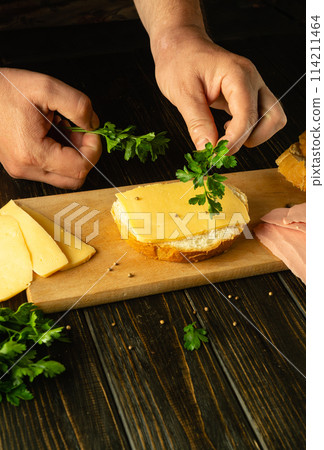 Cooking sandwiches with sausage and cheese on the kitchen table by the hands of a chef. Low key concept of preparing quick food for snacking. Advertising space Cooking sandwiches with sausage and cheese on the kitchen table by the hands of a chef. Low key concept of preparing quick food for snacking. Advertising space 114211464
