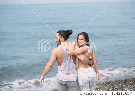 Young fitness couple embracing standing on beach, looking at horizon Young fitness couple embracing standing on beach, looking at horizon 114211697