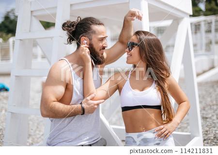 Young couple listening to music using one headphones on beach Young couple listening to music using one headphones on beach 114211831