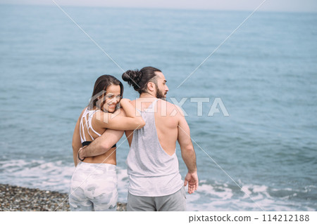 Young fitness couple embracing standing on beach, looking at horizon Young fitness couple embracing standing on beach, looking at horizon 114212188