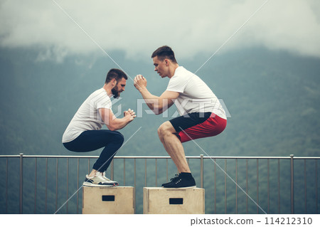 Two male athletic friends doing box jump exercise outdoor 114212310