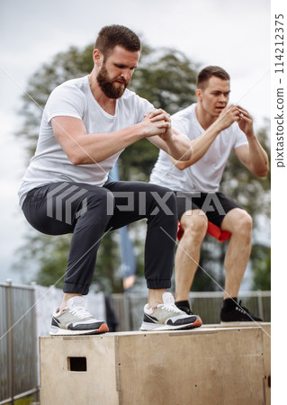 Fit young sportsmen doing box jumps as a group outdoor on top of the mountain Fit young sportsmen doing box jumps as a group outdoor on top of the mountain 114212375
