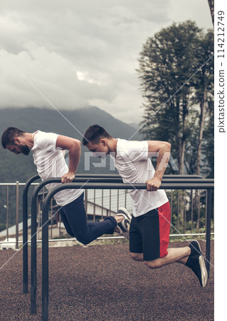 Two sportsmen doing dips on parallel bars Two sportsmen doing dips on parallel bars 114212749