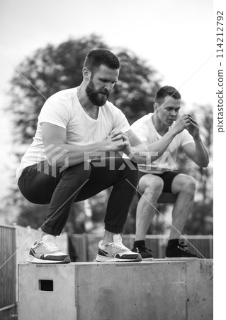Caucasian male athletic friends doing box jump outdoor on top of the mountain. 114212792